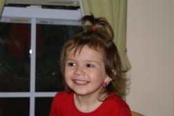 A young girl in a red shirt smiles while looking away from the camera.
